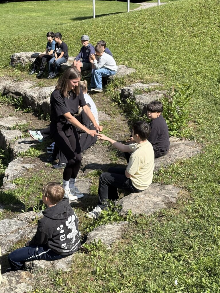 Kinder sitzen auf Steinen im Freien und spielen ein Spiel.