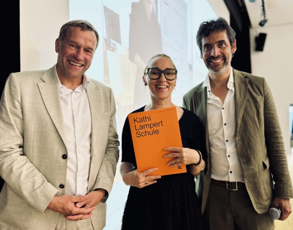 Landesvolksanwalt Klaus Feuerstein und Schulleiter Christoph Schindegger stehen neben einer Studierenden, die das Diplom eine einem orangen Umschlag in den Händen hält.