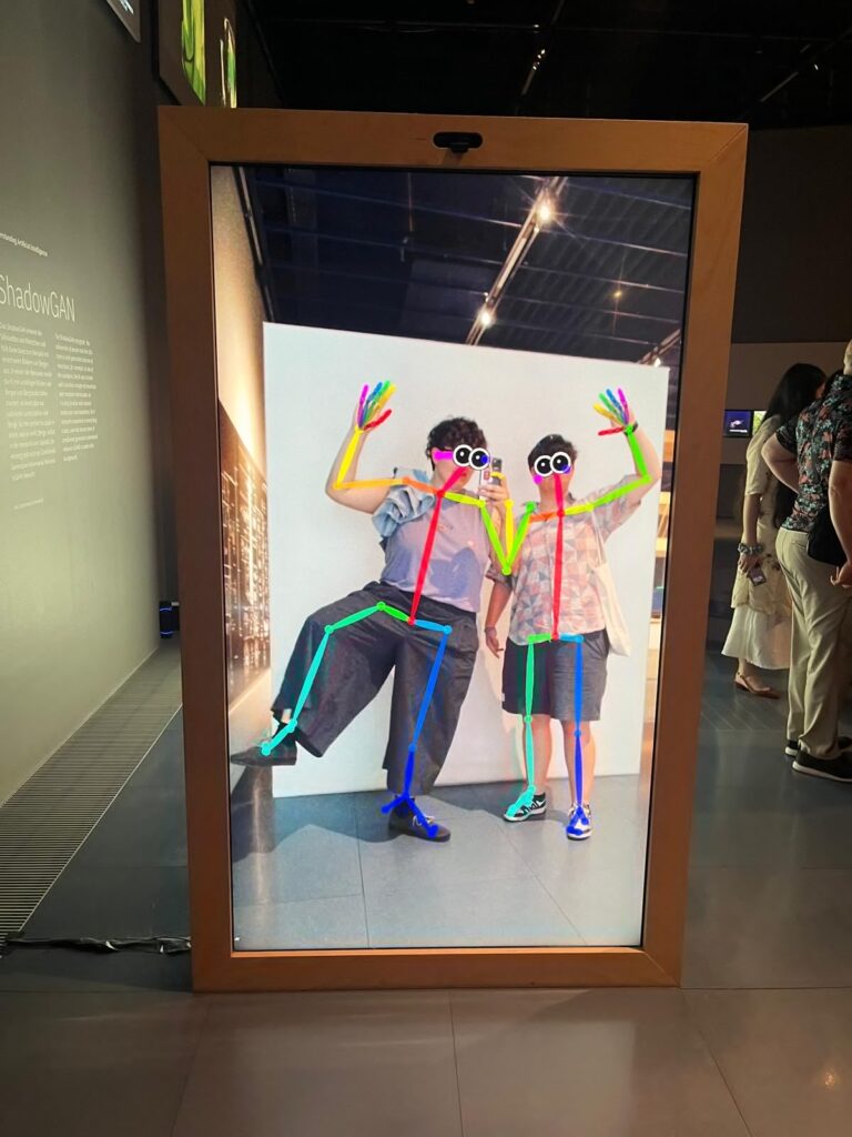 Zwei Personen stehen vor einem Spiegel im Museum und in ihre Körper sind farbige Striche projeziert.